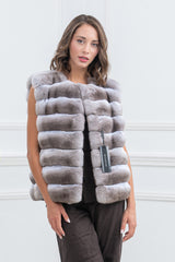 Dark beige chinchilla fur vest with a sleeveless, hip-length silhouette and horizontal panels, shown front-facing with a MANZARI brand tag.