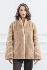 A short palomino mink fur jacket with a shawl collar. The sleeves feature horizontal banded construction, while the body panels are vertical.