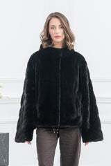 Front view of a short black mink jacket with a high collar, straight silhouette, and wide sleeves. Features a hidden closure and drawstring hem.