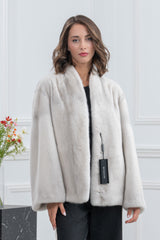 Close-up of a collarless cream mink fur jacket with a black branded tag attached to the front closure.
