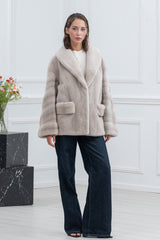 Short pearl blue mink fur jacket with wide lapel collar, horizontal panels on sleeves, and two front pockets, worn over blue jeans.