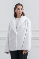 Front view of a white mink fur short jacket with a wide shawl collar, long sleeves, and a straight-cut hem, worn over a white top and dark jeans.