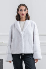 White mink short jacket with a wide shawl collar, featuring horizontal fur panels on the sleeves and a drawstring hem with metallic toggles.
