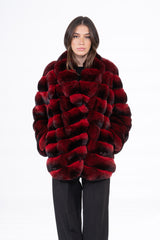A short jacket in red and black chinchilla skin, featuring horizontal panels and a high collar, modeled from the front against a white backdrop.
