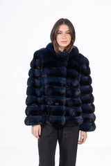A blue black chinchilla short jacket with horizontal fur panels, a round collar, and long sleeves, worn over black trousers.