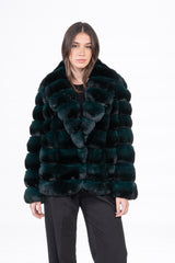 A short, deep emerald chinchilla jacket featuring horizontal panels and a wide lapel collar, worn over a black top and black trousers.