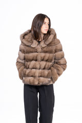 Russian sable short jacket in taupe with horizontal fur banding and a large hood, worn over black trousers.