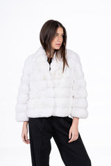 Snow white chinchilla short jacket with horizontal fur panels, long sleeves, and a folded collar, worn open over black trousers.