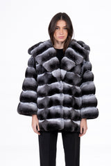 Front view of a chinchilla fur jacket with a large hood and horizontal panels in a high-contrast grey, black, and white gradient pattern.