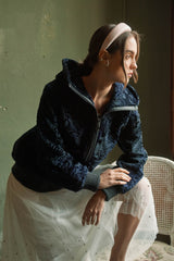 Blue-black astragan fur short jacket featuring a hood, ribbed cuffs and hem, and a front zip closure with leather trim detail.