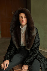 A black Swakara long jacket with a large brown sable hood. The Swakara fur has a rippled, flat texture and the sable hood is plush and thick.