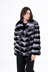 Short chinchilla jacket featuring a V-chevron pattern in grey, white, and black fur with a wide collar, worn over a black top and trousers.