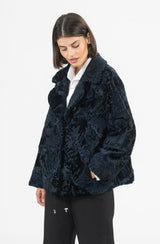 Short dark navy Swakara fur jacket with a classic collar, worn over a white shirt, featuring a subtle chevron texture.